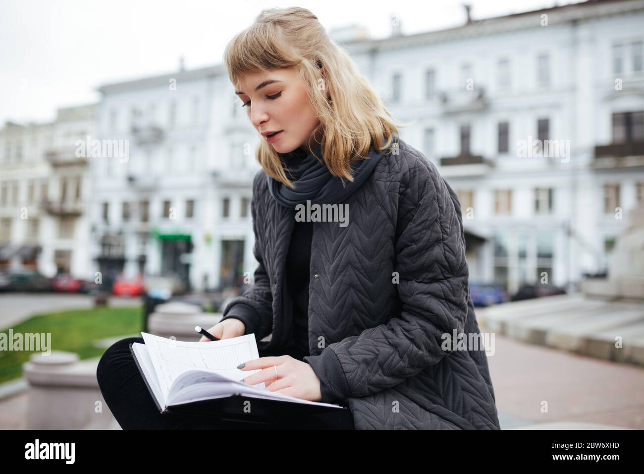 Schönes Mädchen mit blonden Haaren sitzen mit Notebook in der Hand auf der Straße der Stadt Stockfoto