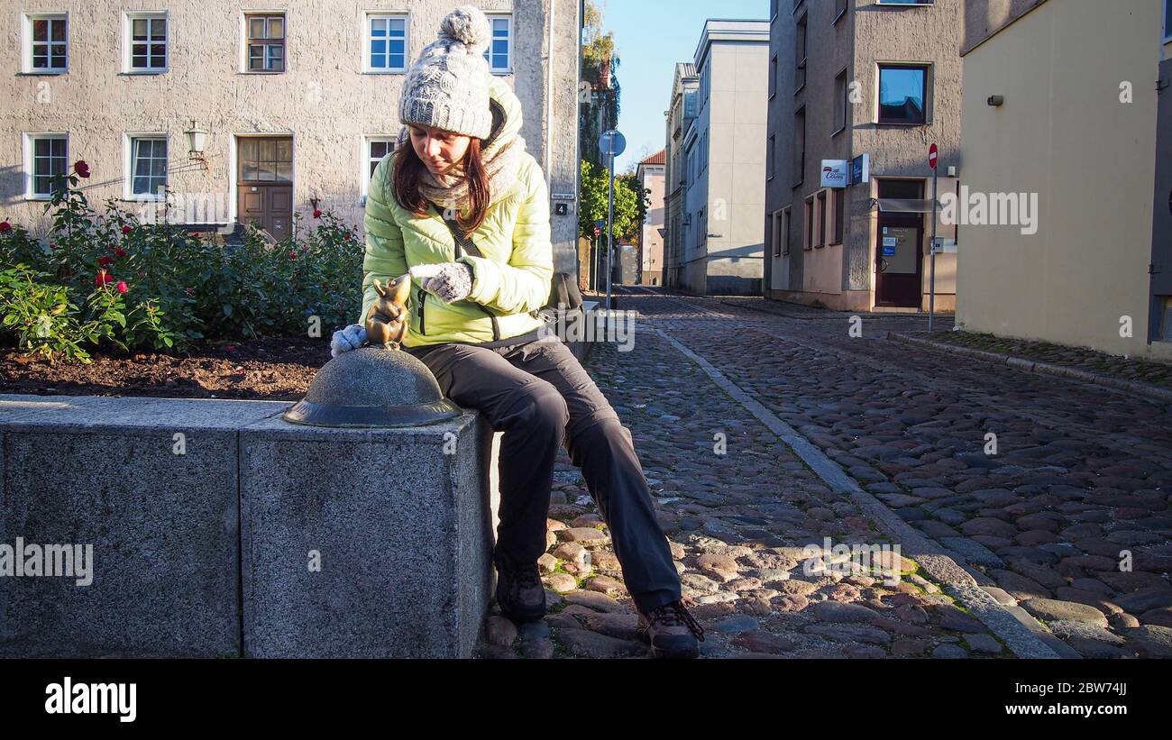 KLAIPEDA, LITAUEN - 15. OKTOBER 2019: Touristenmädchen mit der Bronzeskulptur "Steinlingas peliukas" (wundervolle kleine Maus) (entworfen von Svajunas Jur Stockfoto