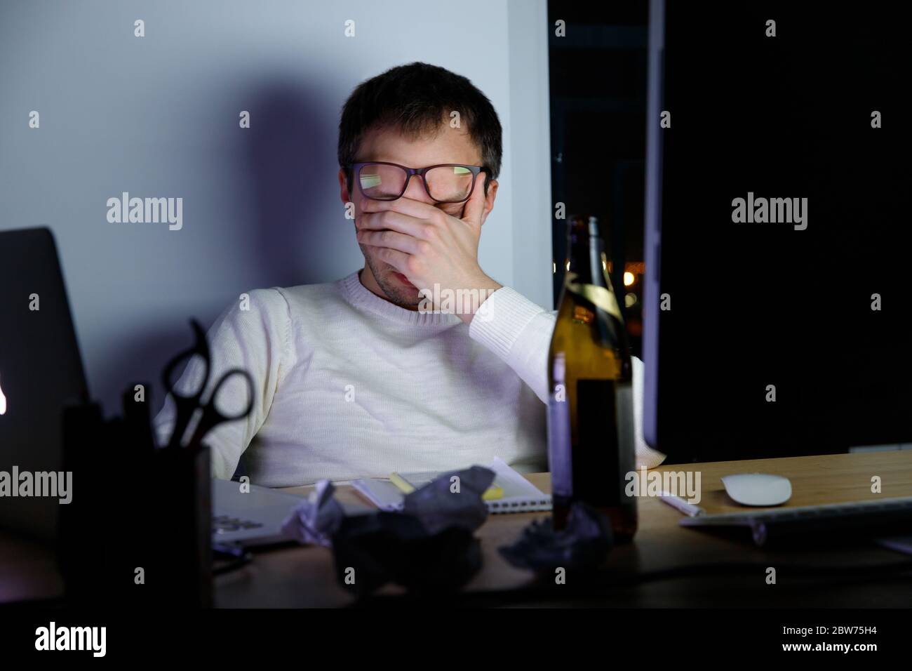 Erschöpfter junger Mann in Gläsern, der in einer späten Nacht bei der Arbeit Strapazen erlebt, trank ein Bier, um sich zu entspannen, schläft vor Müdigkeit ein. Überarbeit, Faulheit, Stockfoto