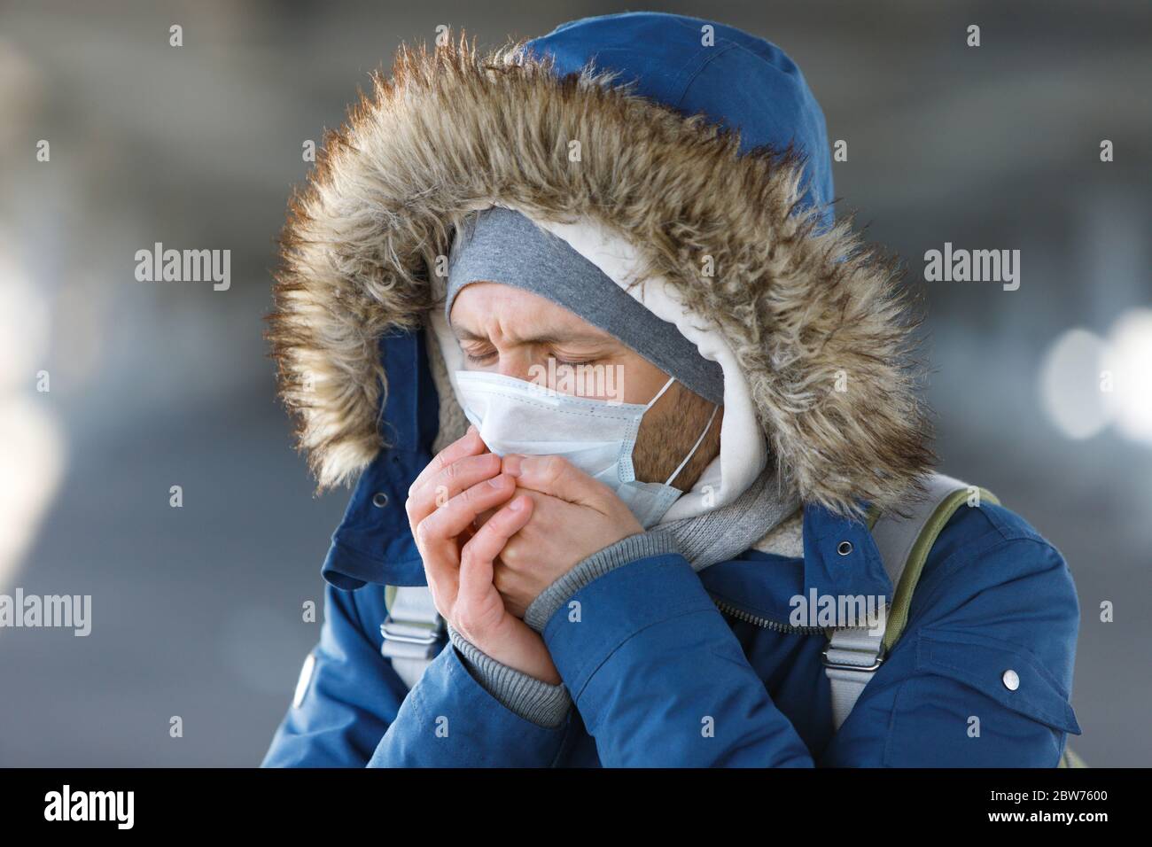 Nahaufnahme eines kranken jungen Mannes, der eine Erkältung hat, niest, hustet und eine medizinische Gesichtsmaske trägt, im Freien. Bronchitis, Krankheit, Grippeepidemie Stockfoto