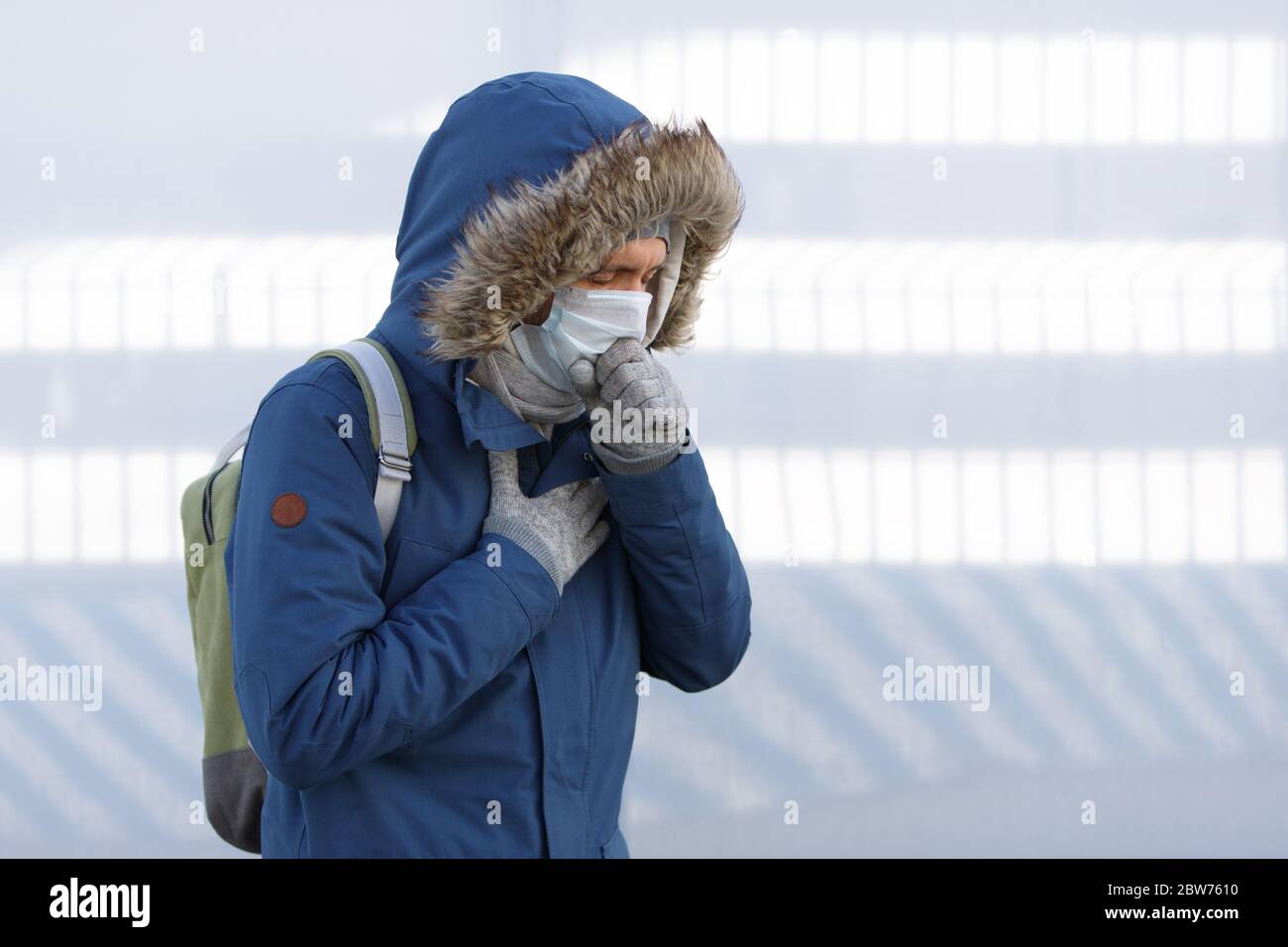 Kranker junger Mann, der eine Erkältung hat, sich unwohl fühlt, niest, hustet und eine medizinische Gesichtsmaske trägt, im Freien. Bronchitis, Krankheit, Grippeepidemie Stockfoto