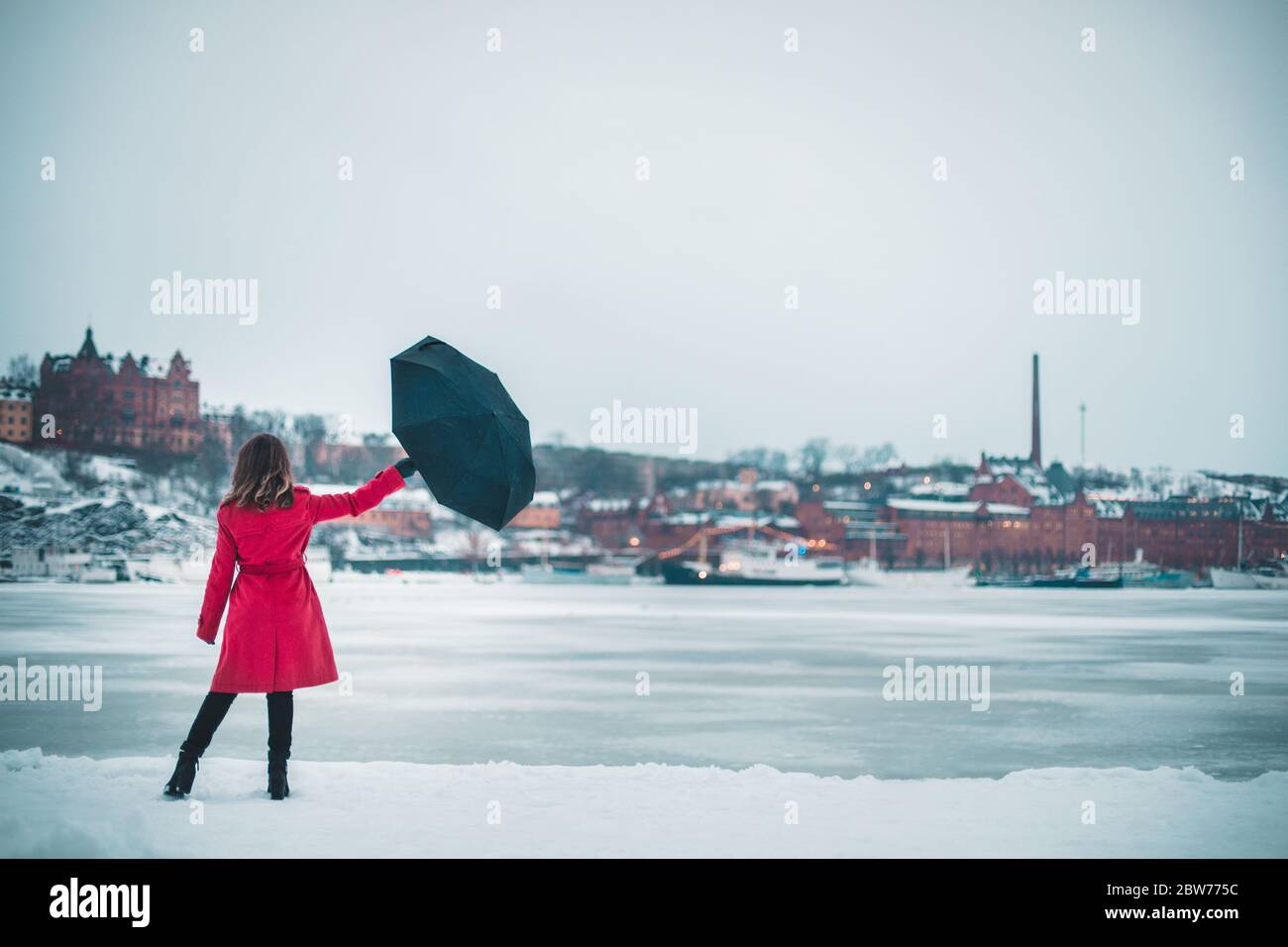 Eine Frau, die einen roten Regenschirm an einem zugefrorenen See in Stockholm hält Stockfoto