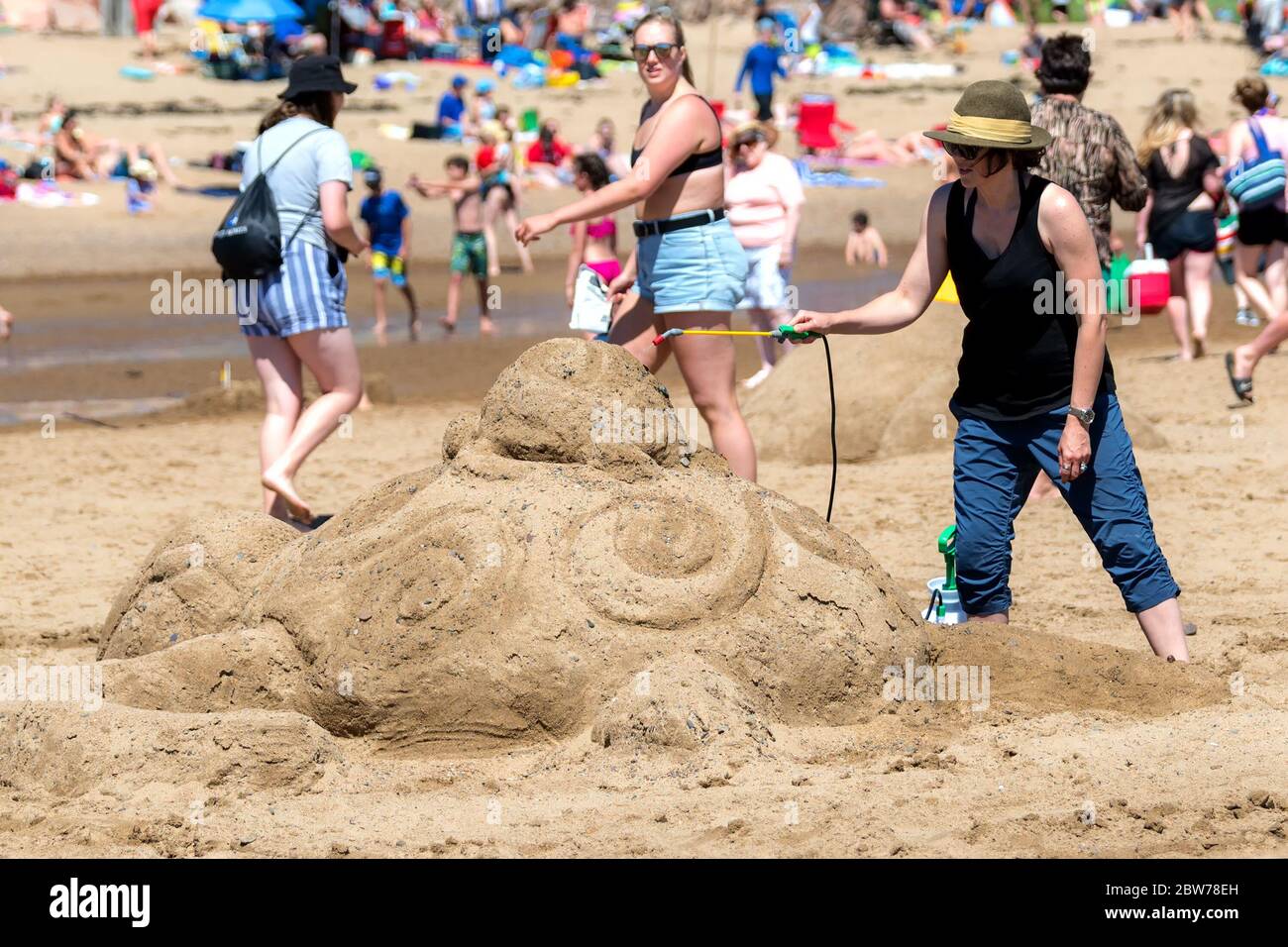 New River Beach, New Brunswick, Kanada - 7. Juli 2018: Der jährliche Wettbewerb für Sandskulpturen. Eine Frau sprüht Wasser auf eine Skulptur von Mutter und Baby Stockfoto