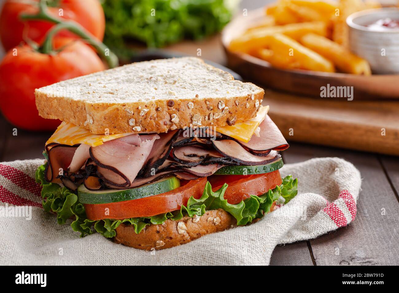 Nahaufnahme eines Schinken-Käse-Sandwich mit Salat, Tomaten und Gurken auf Vollkornbrot auf einem Holztisch Stockfoto