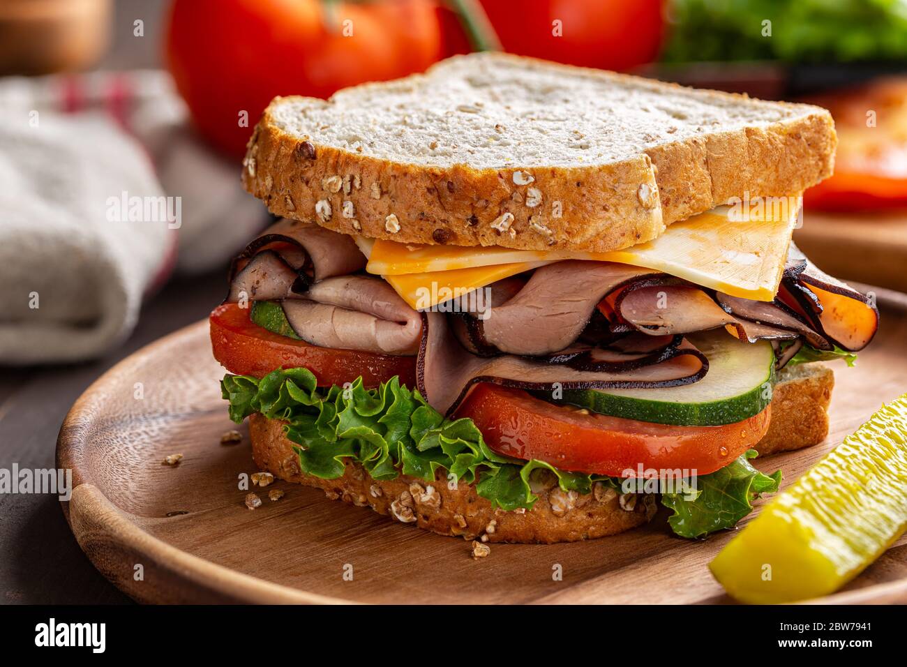 Nahaufnahme eines Schinken-Käse-Sandwich mit Salat, Tomaten und Gurken auf Vollkornbrot auf einem Holzteller Stockfoto