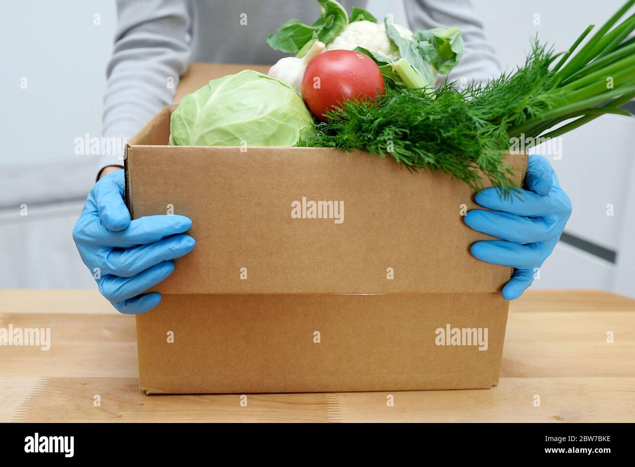 Volunteer in Handschuhen hält Lebensmittel Spende Box Gemüse, um die Armen zu helfen. Donat-Box mit Lebensmitteln Stockfoto