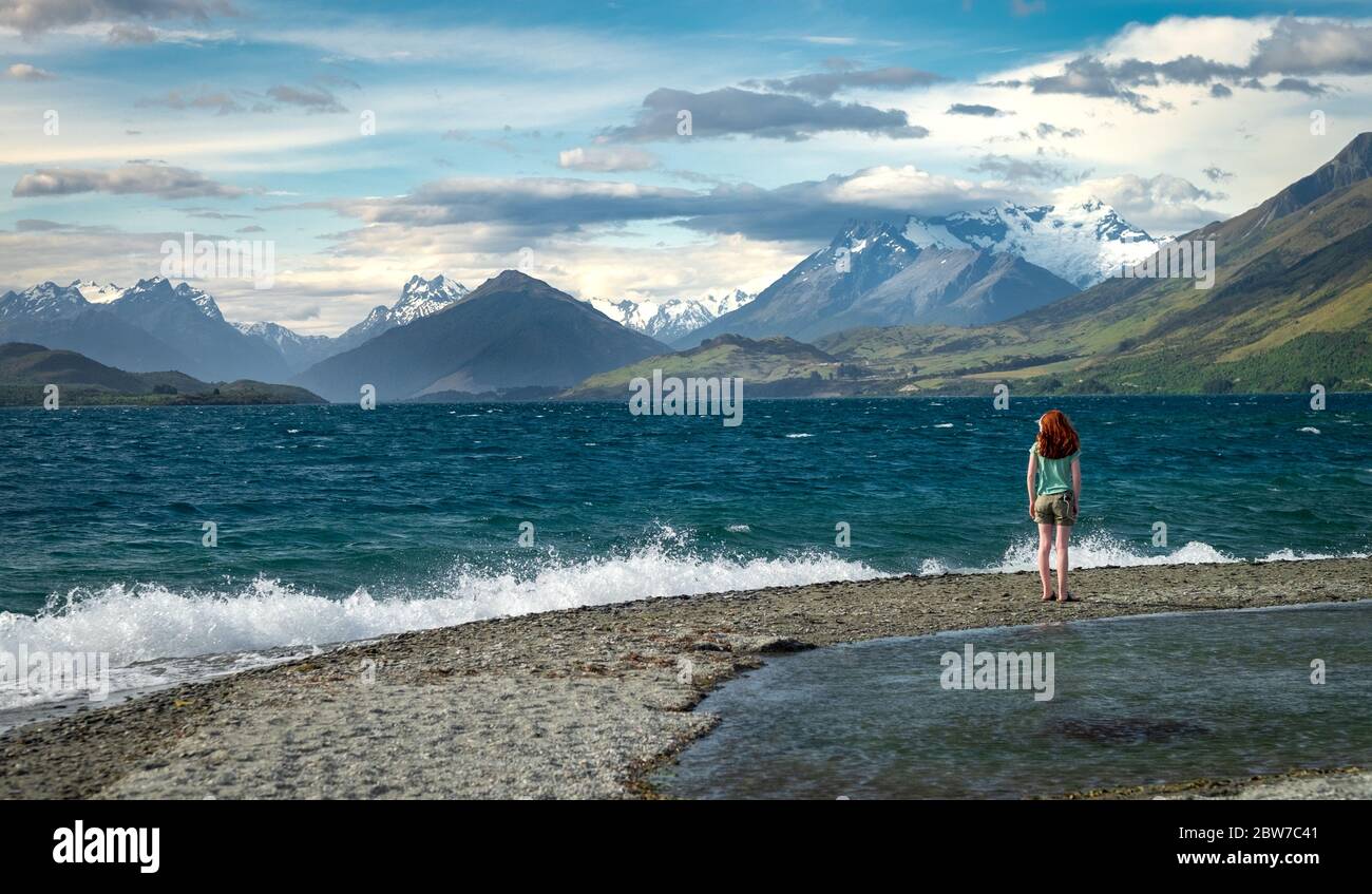 Junges Mädchen mit Headset am Ufer des Lake Wakatipu auf der Südinsel Neuseelands. Blick auf die Humboldt-Berge in der Ferne Stockfoto