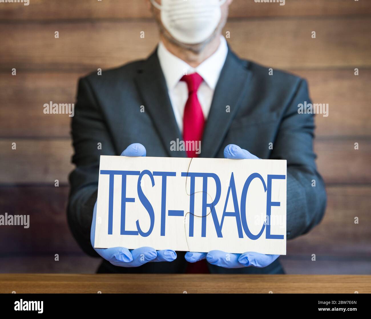 Ein Arzt, Geschäftsmann oder Arbeitgeber, der persönliche Schutzausrüstung trägt, Gesichtsmaske und blaue Handschuhe und ein Schild, das die Öffentlichkeit zum Testen und Trace auffordert Stockfoto