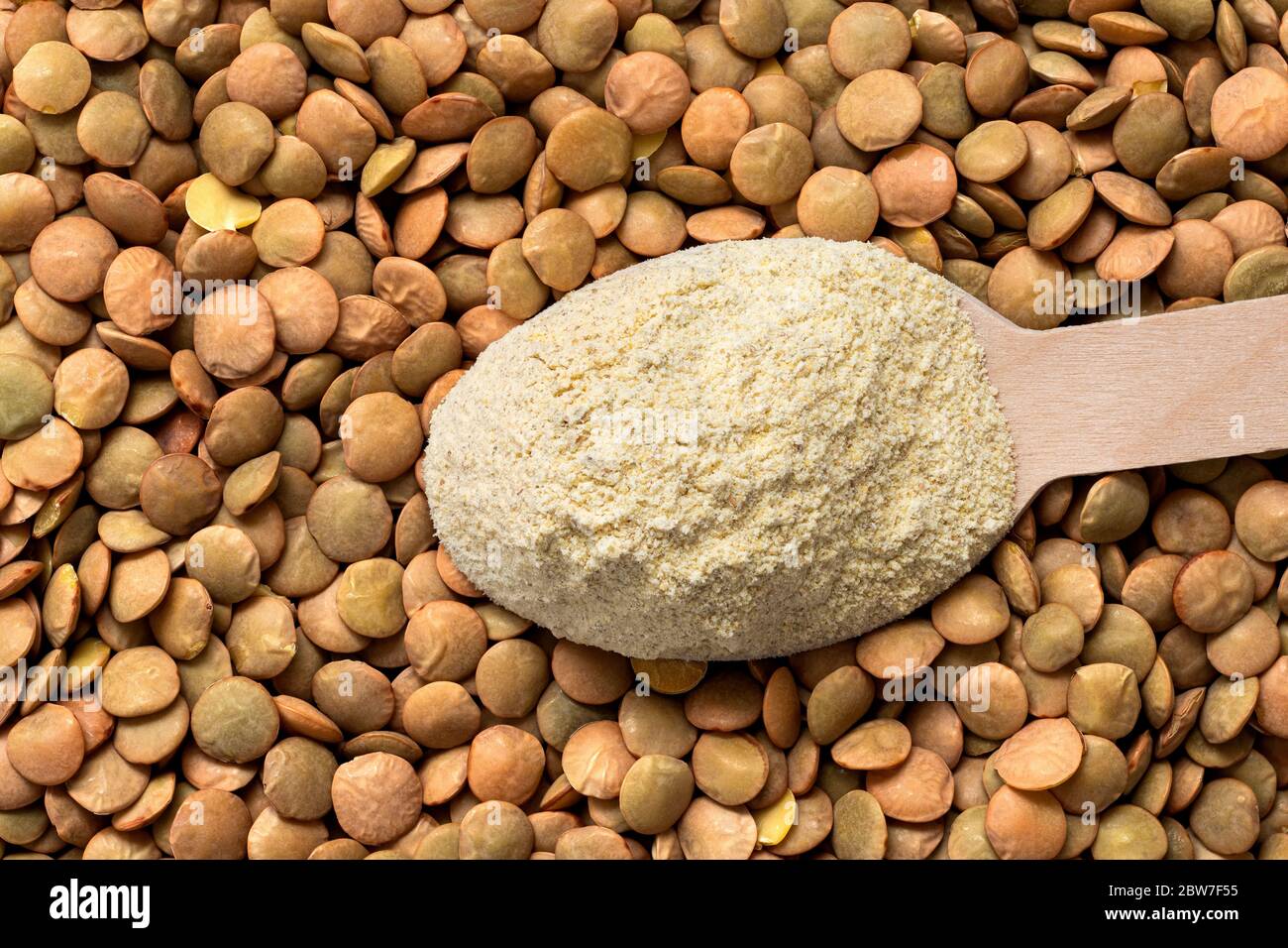 Holzlöffel getrocknetes Linsenmehl auf getrockneten braunen Linsen. Draufsicht. Stockfoto