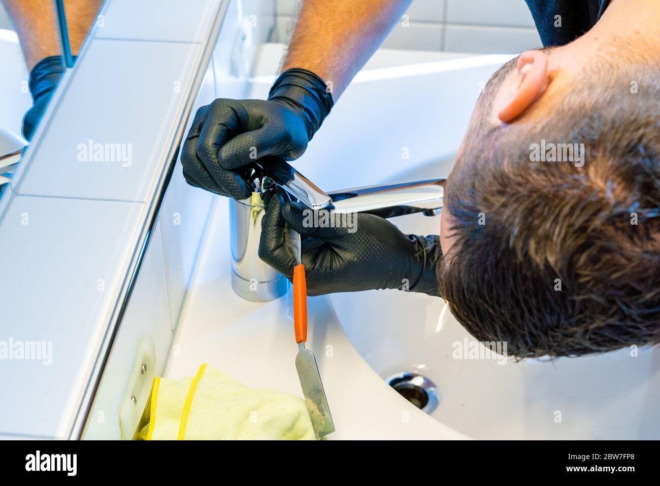 Ein professioneller Reiniger Entkalken ein Waschbecken Wasserhahn mit einem Schaber und Kalk Pick vor dem Finishing und Polieren Stockfoto