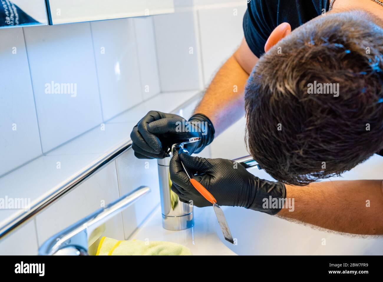 Ein professioneller Reiniger Entkalken ein Waschbecken Wasserhahn mit einem Schaber und Kalk Pick vor dem Finishing und Polieren Stockfoto