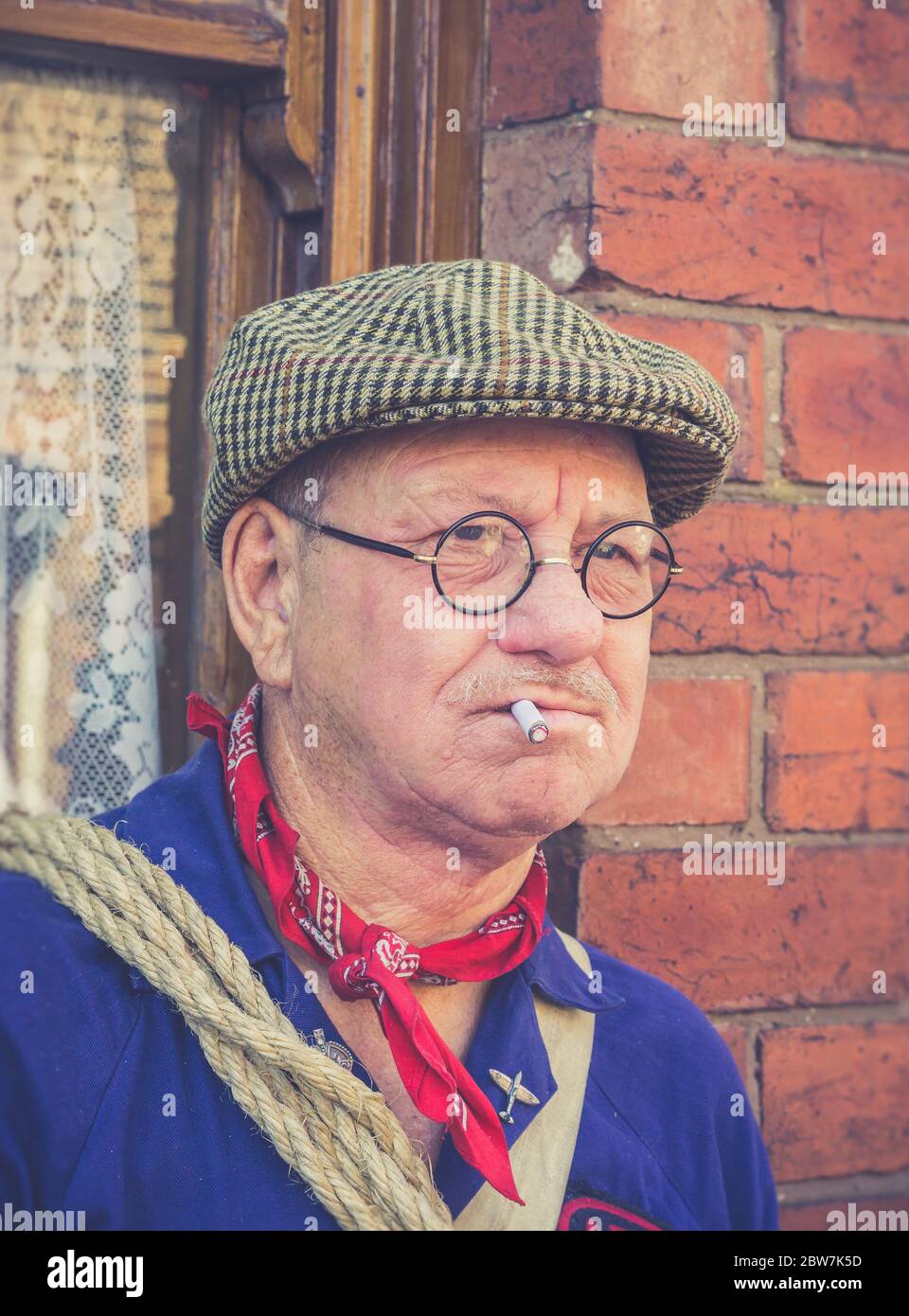 Nahaufnahme eines ARP-Mannes aus den 40er Jahren mit flacher Kappe und Zigarette im Mund, isoliert im Freien, Ereignis des zweiten Weltkriegs, Großbritannien. Mann aus dem 2. Weltkrieg, der mürrisch raucht. Stockfoto