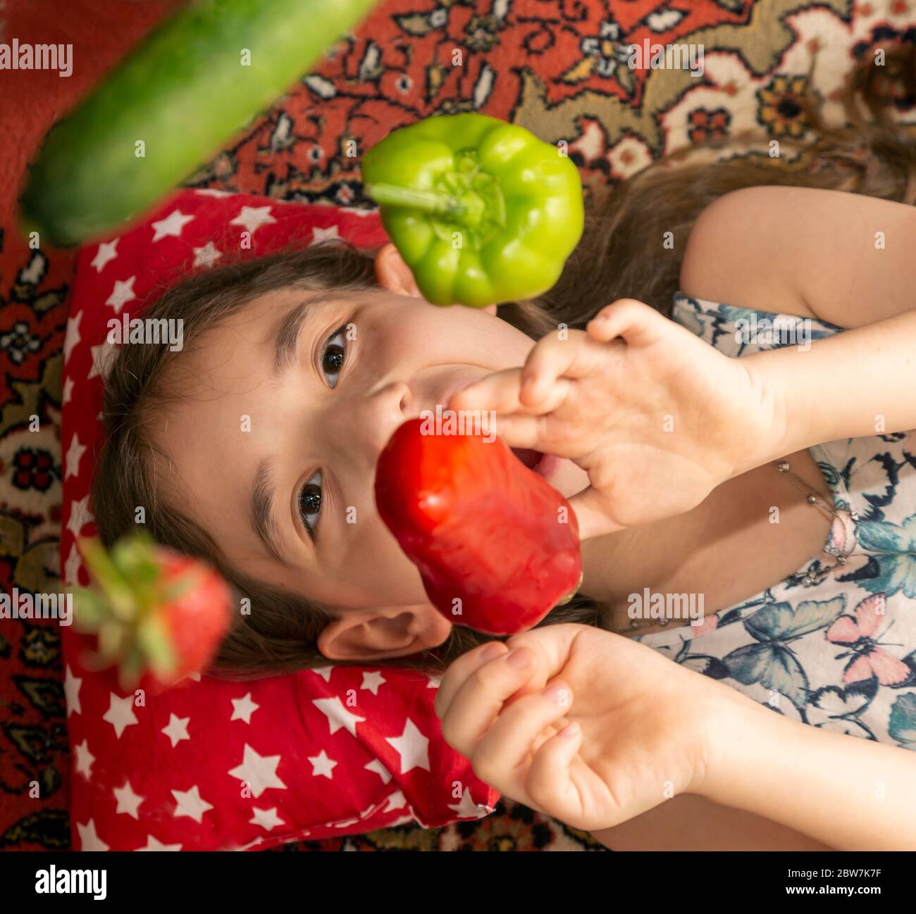 Das Kind spielt mit Fliegengemüse. Ein kleines Mädchen spielt mit rotem Pfeffer, Gurke, Erdbeere, Kiwi grünen Pfeffer und Zitrone in ihrem Haus Stockfoto