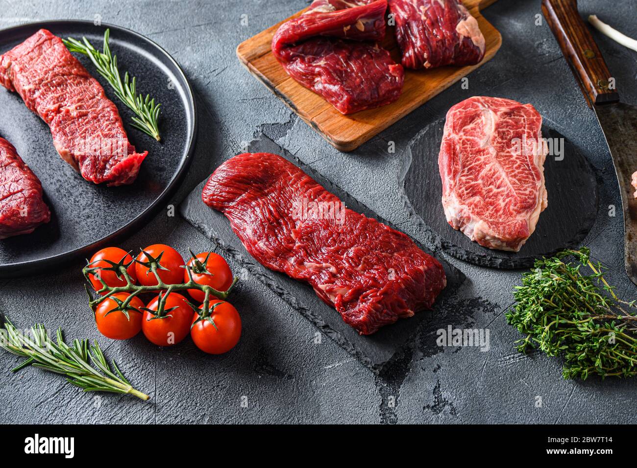 Bio denver, Top Blade, Tri Tip Steak auf einem schwarzen Teller und Steinschiefer mit Gewürzen, Kräuter grau Beton Hintergrund. Seitenansicht. Stockfoto