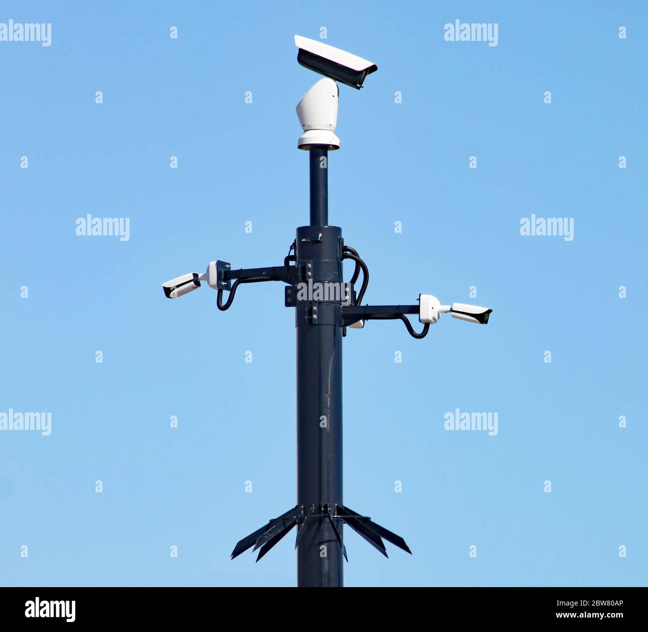 Überwachungskameras auf einem schwarzen Pfosten halten den Verkehr in einem Stadtzentrum im Auge. Der Hintergrund ist ein klarer blauer Himmel. Metallspitzen verhindern pe Stockfoto