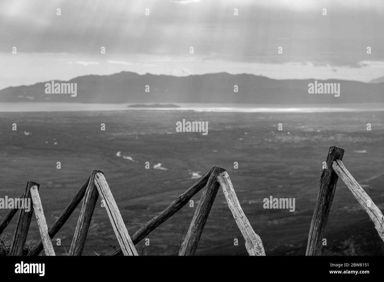 Holzzaun hoch in Bergen mit verschwommenen Sonnenstrahlen durch schwere Wolken über dem Meer in Nordgriechenland. Blick aus dem Hochwinkel von den Bergen in der griechischen Region Xanthi. Reisefoto in Schwarz und Weiß Stockfoto