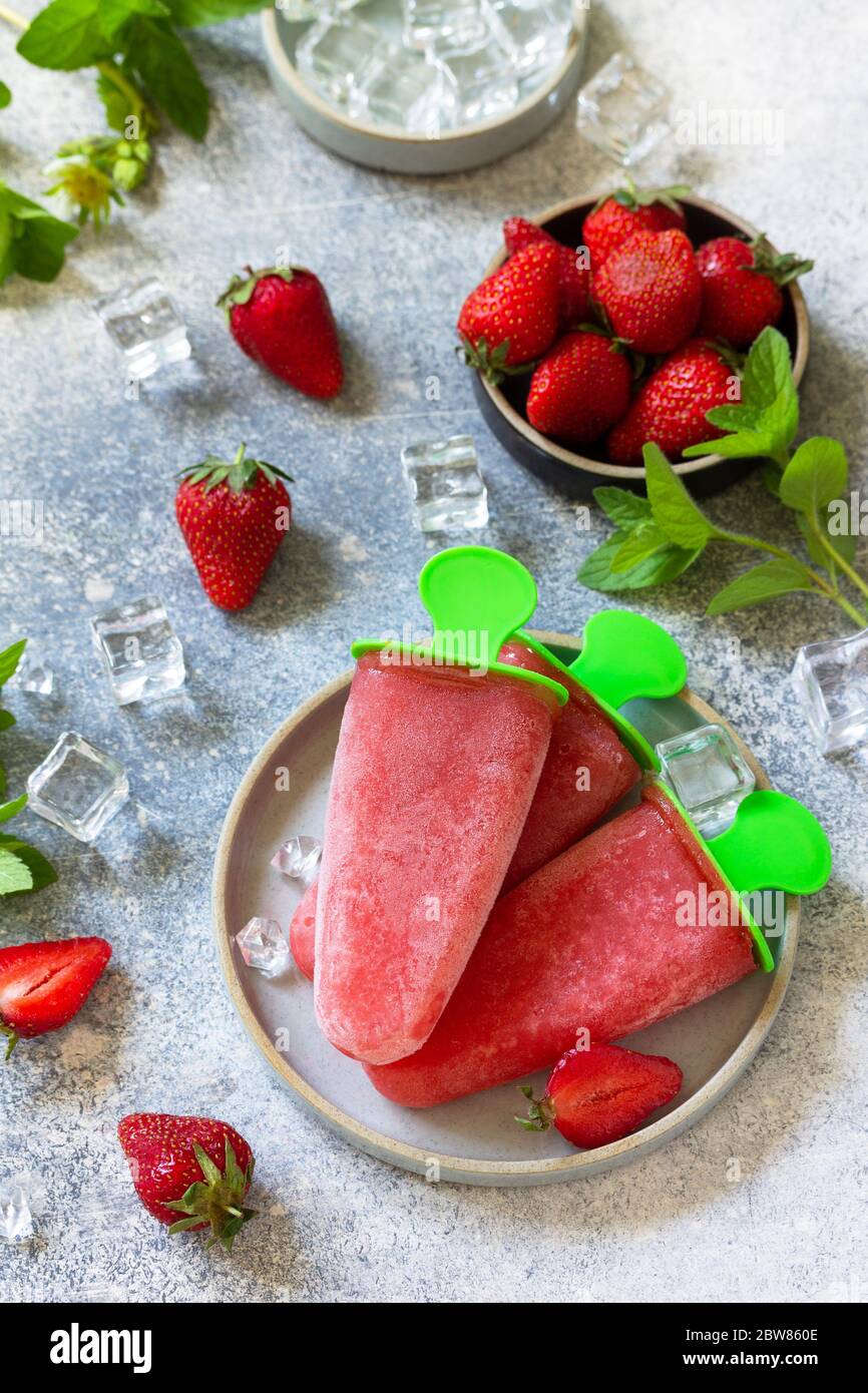 Selbstgemachter Erdbeer-Fruchtsaft. Eis oder Eiszapfen auf einem hellen Stein- oder Schiefertisch. Stockfoto