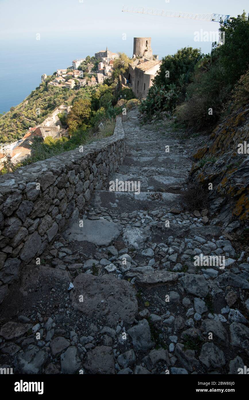 Ein Pfad von unebenen abgebrochenen Stufen führt hinunter einen Hügel mit alten Befestigungsanlagen und eine entfernte Stadt am Rande eines trüben blauen Meeres Stockfoto