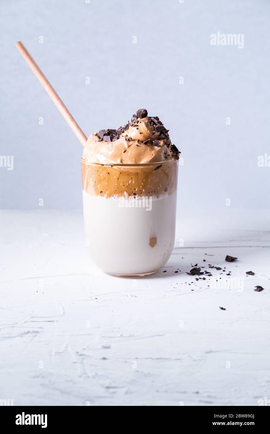 Dalgona Kaffee im Glas mit Schokoladenstückchen und Bambusstroh auf weißem Hintergrund. Vertikales Bild. Stockfoto