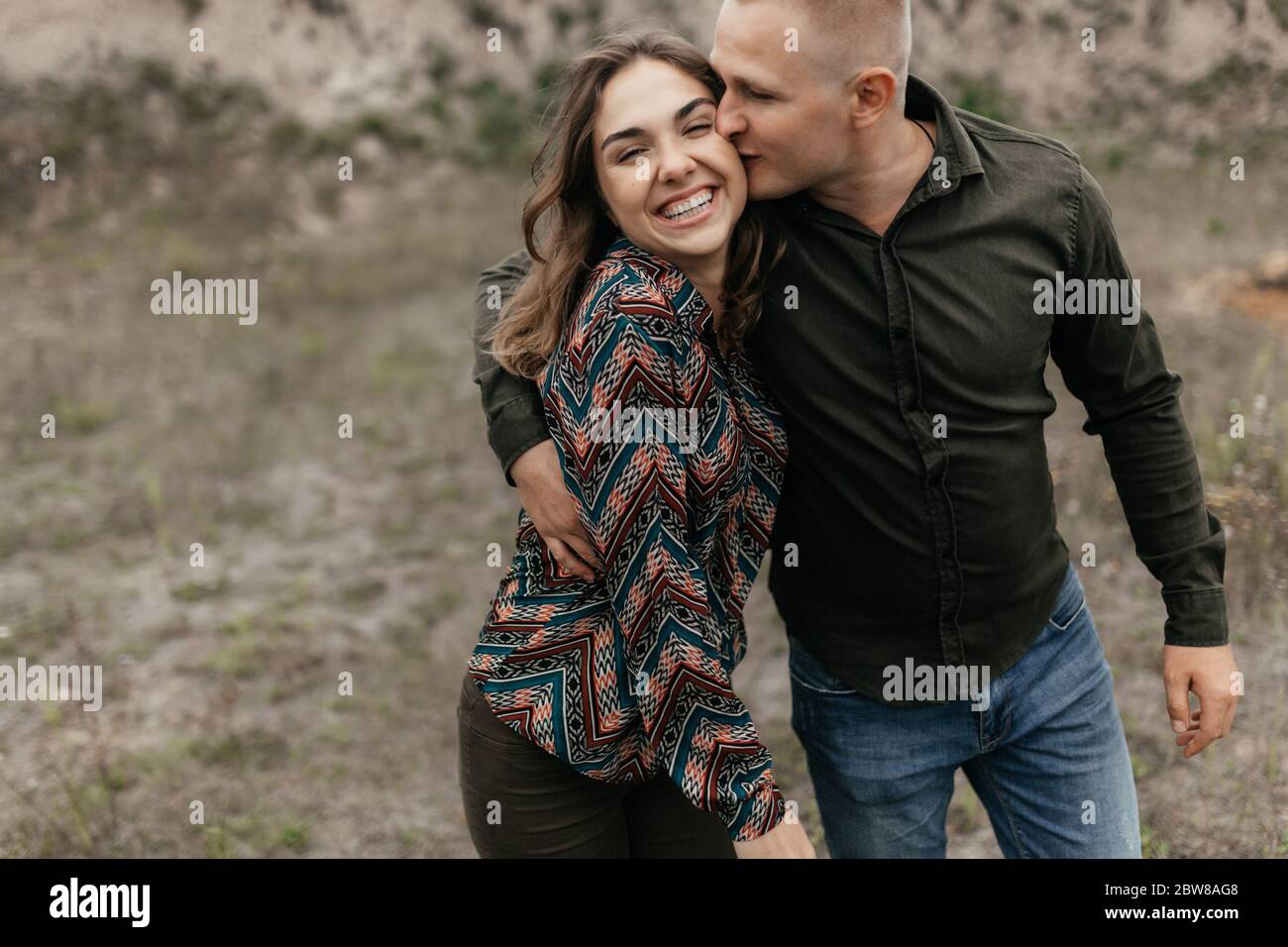 Mann küsst seine lächelnde Frau, während er in der Natur geht. Glückliches Paar Stockfoto