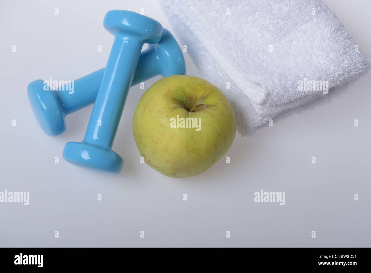 Barbells klein neben Apple Obst, Ansicht von oben. Hanteln aus Kunststoff blau in der Nähe von weichen Handtuch auf weißem Hintergrund. Gesunder Lebensstil und Sport Konzept. Gesundheit und Fitness Symbole Stockfoto
