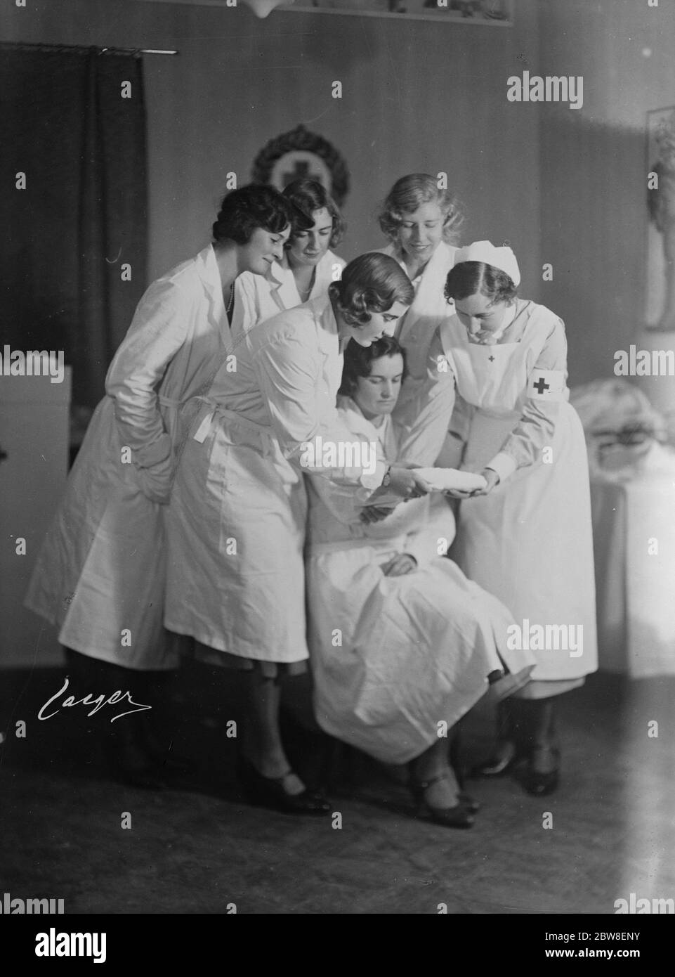 Prinzessin Ingrid unter einem roten Kreuz natürlich . Prinzessin Ingrid von Schweden (in der Mitte) mit Kommilitonen beobachten die Krankenschwester zu demonstrieren, wie man eine Kompresse anwenden. Dezember 1930 Stockfoto