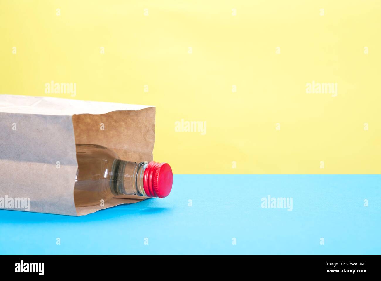 Papiertüte mit einer Flasche Alkohol auf gelbem und blauem Hintergrund Stockfoto