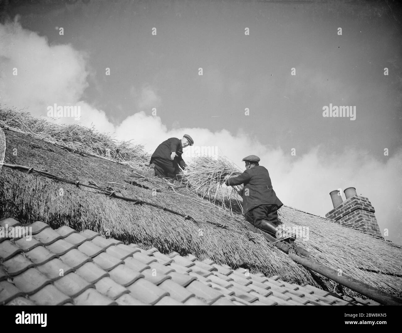 Männer arbeiten auf einem Ziegeldach und setzen Strohhalm auf dem Dach eines Cottage in Orpington. 1935 . Stockfoto