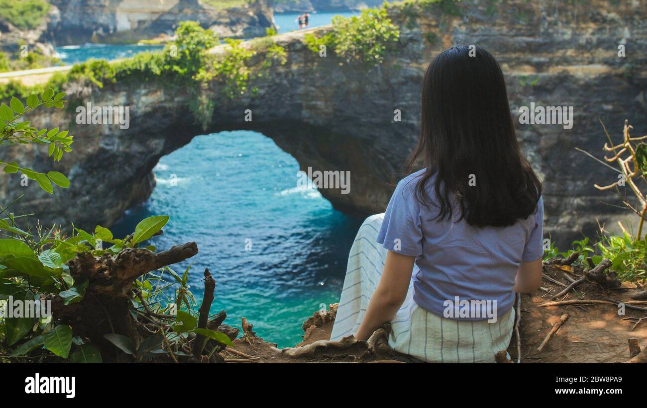 Rückansicht Frau am Rande einer Klippe Blick auf gebrochenen Strand. Broken Beach Nusa Penida. Indonesien. Stockfoto