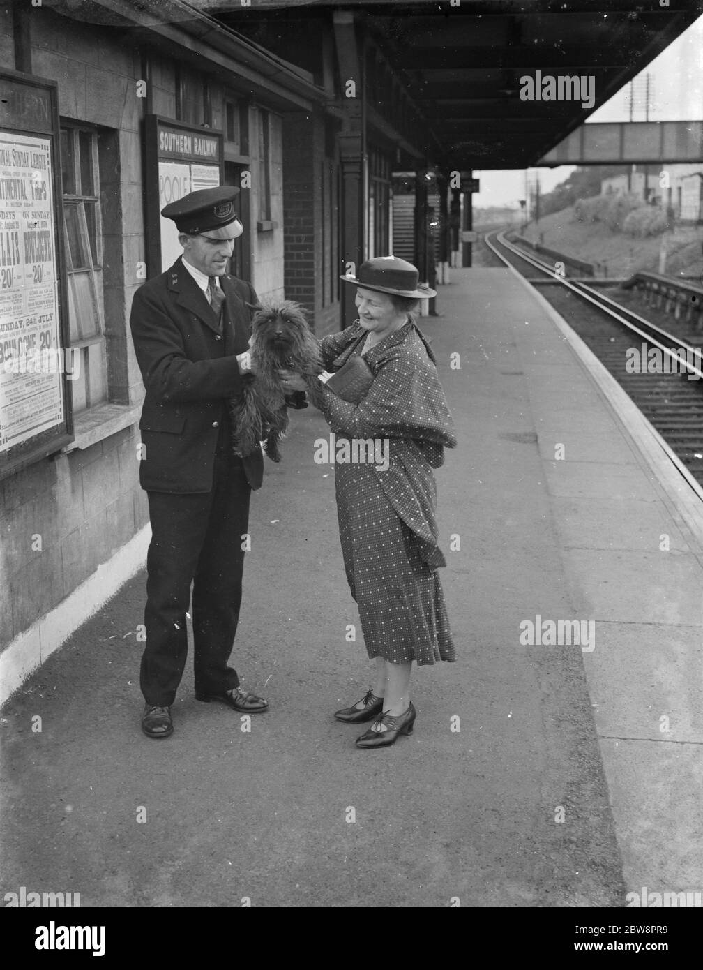 Ein glücklicher Hund wird von einem Bahnhofswärter mit Frau Boune Williams, nachdem er dem Tod in Orpington entkommen, hoch gehalten. 1938 Stockfoto
