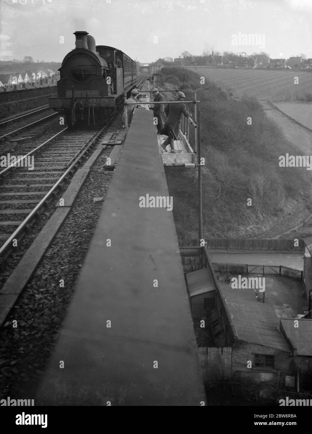 Eisenbahner stehen auf einem Gerüst am Rande des Viadukts, wie eine Dampfmaschine passiert, wie sie Reparaturen auf der Strecke in South Darenth, Kent. 1938 Stockfoto