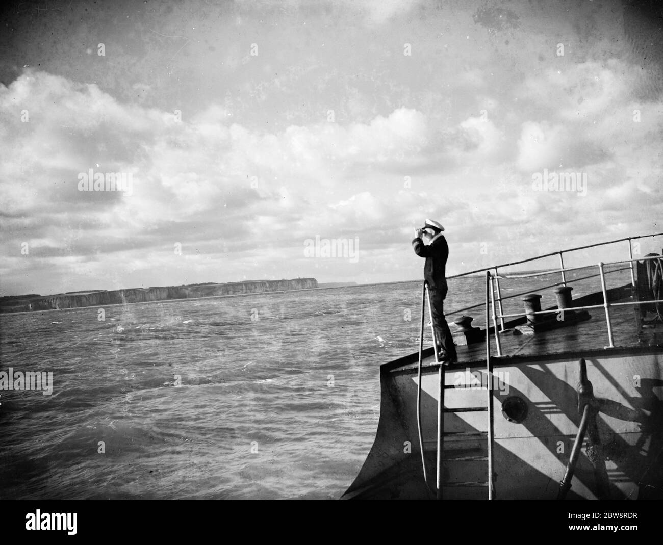 Der Kapitän schaut durch sein Fernglas vom Deck des Tramp-Damasters der , ' SS Eston ' auf die Küste Frankreichs. 1935 Stockfoto
