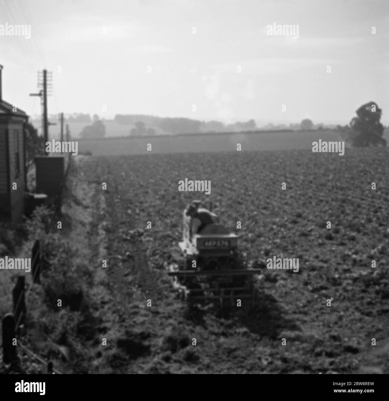 Ein Bauer auf einem Traktor, der ein Feld pflügt. 1936 Stockfoto