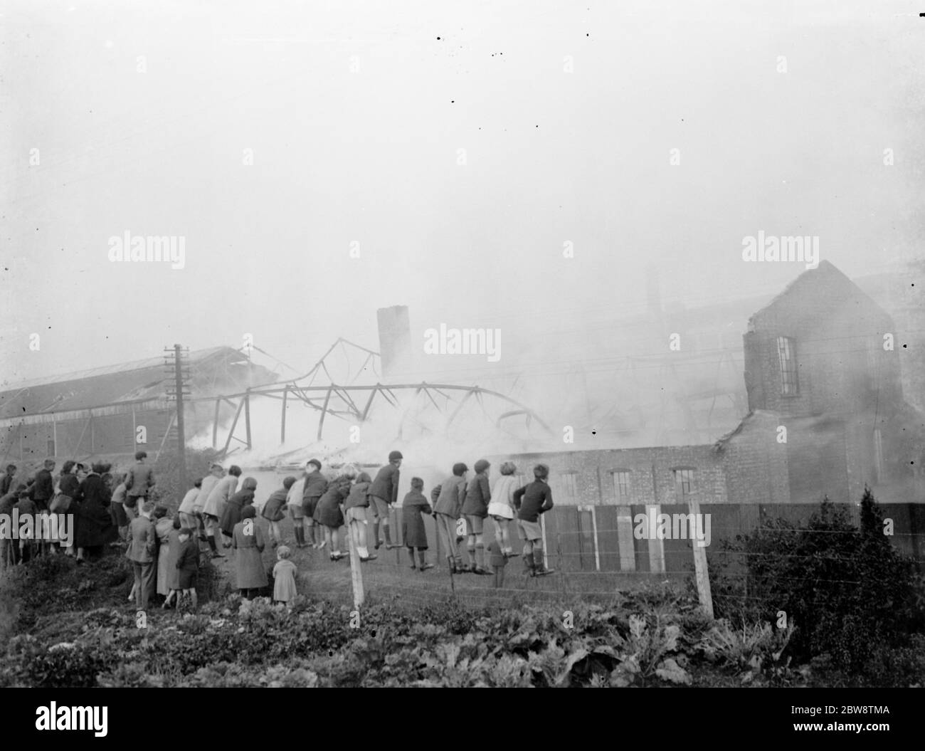 Kinder klettern auf einen Zaun, um das Feuer in der Vickers Fabrik in Crayford, Kent zu beobachten. 1936 Stockfoto