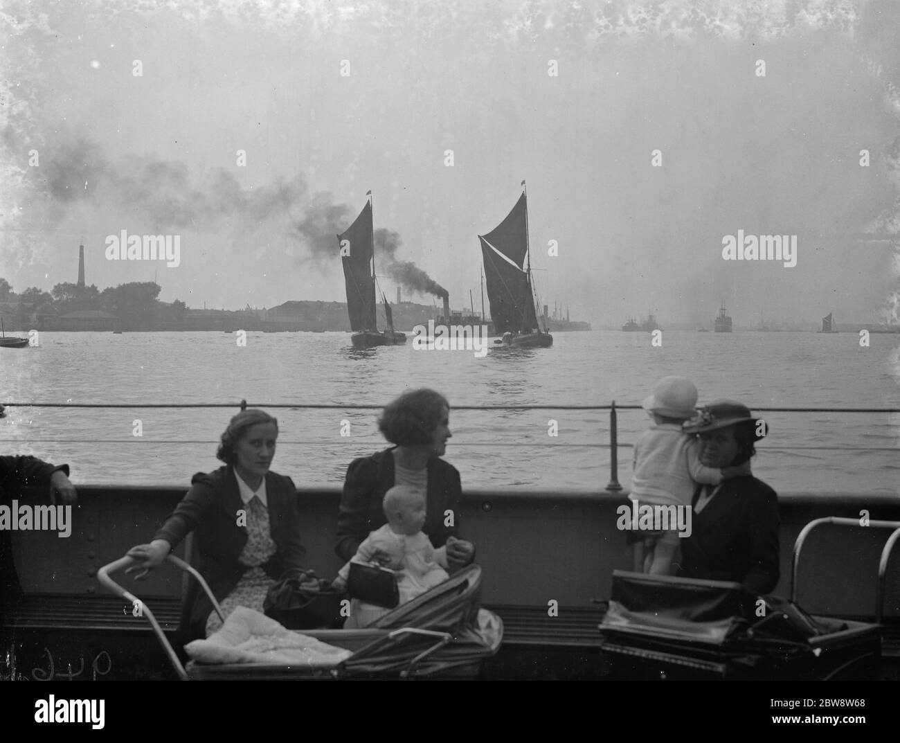 Mütter mit ihren Babys auf einem Boot vor der Kulisse der Themse Lastkähne auf dem Fluss . 1938 Stockfoto