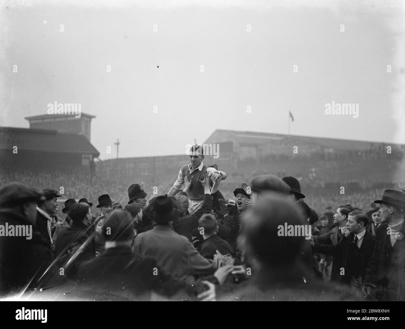Dave Mango, der Kapitän von Millwall, wird von den Massen, die den Platz geschwommen haben, nach dem FA Cup Sieg von Millwall gegen die Favoriten, Manchester City, im Stadion "The Den" in New Cross, London, hoch getragen. Magnall erzielte die beiden Tore, die Millwall durch das Viertelfinale nahm. 1937 Stockfoto