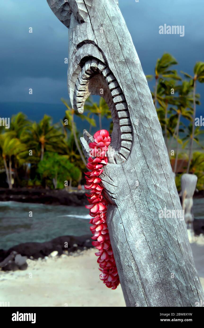 Wunderschöne rosa Plumeria lei hängt von der offenen Mündung eines hawaiianischen Tiki im Puuhonua o Honaunau National Historical Park auf der Big Island von Hawaii. Stockfoto