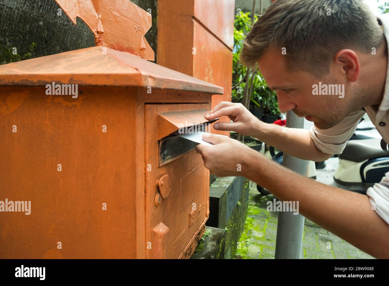 Mann, der einen Brief in einem roten Briefkasten für seine Eltern im Urlaub postiert. Stockfoto