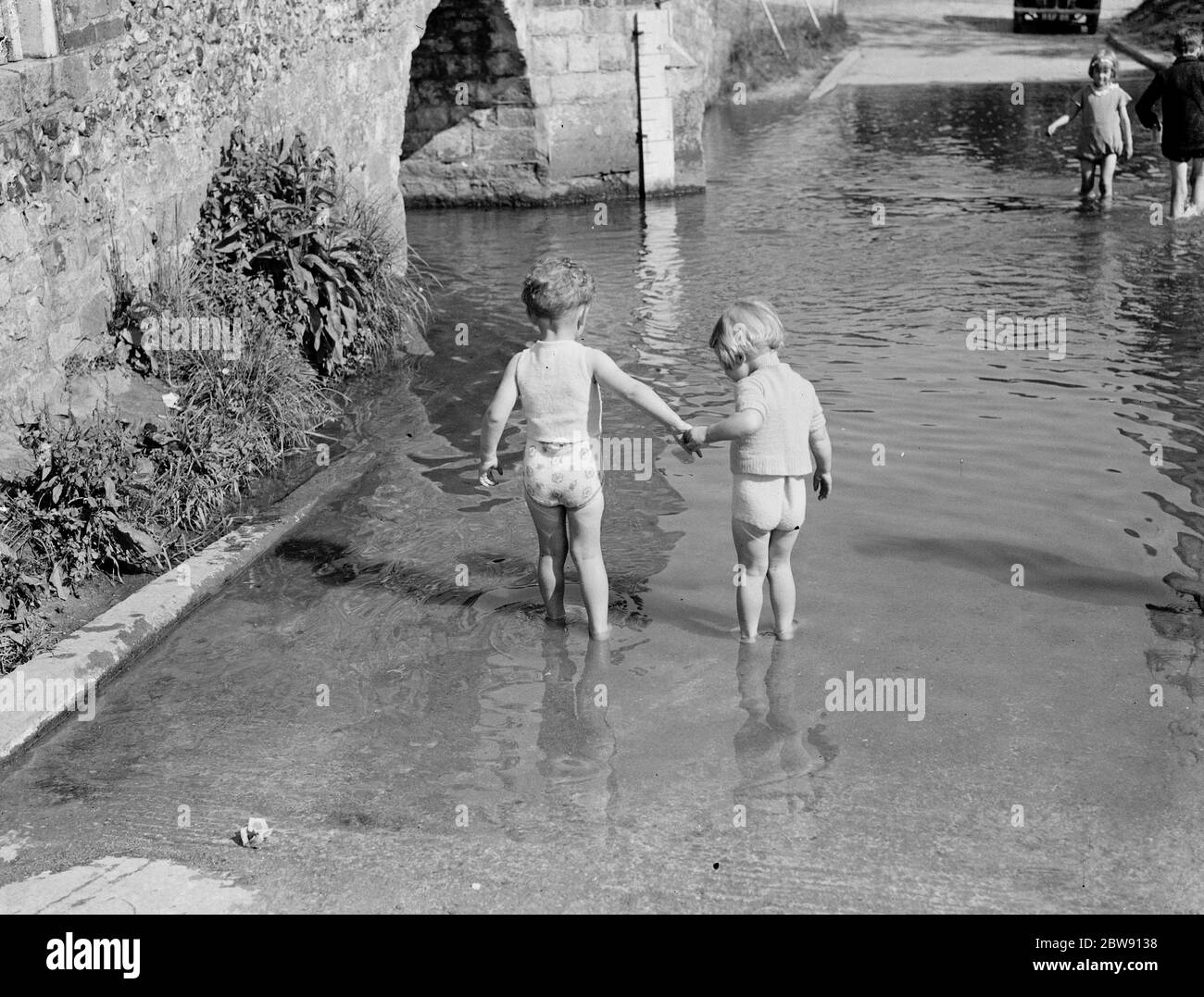 Kleine Kinder paddeln in der ford an der Buckelbrücke von Eynsford über den Fluss Darent in Kent. 1939 . Stockfoto