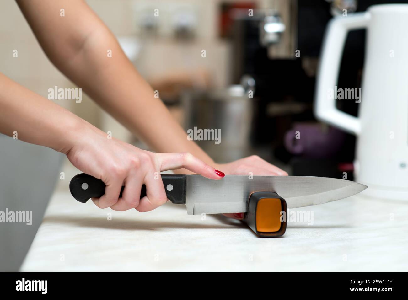 Eine einsame Frau macht Männerarbeit und schärft mit einem Spitzer ein Messer Stockfoto