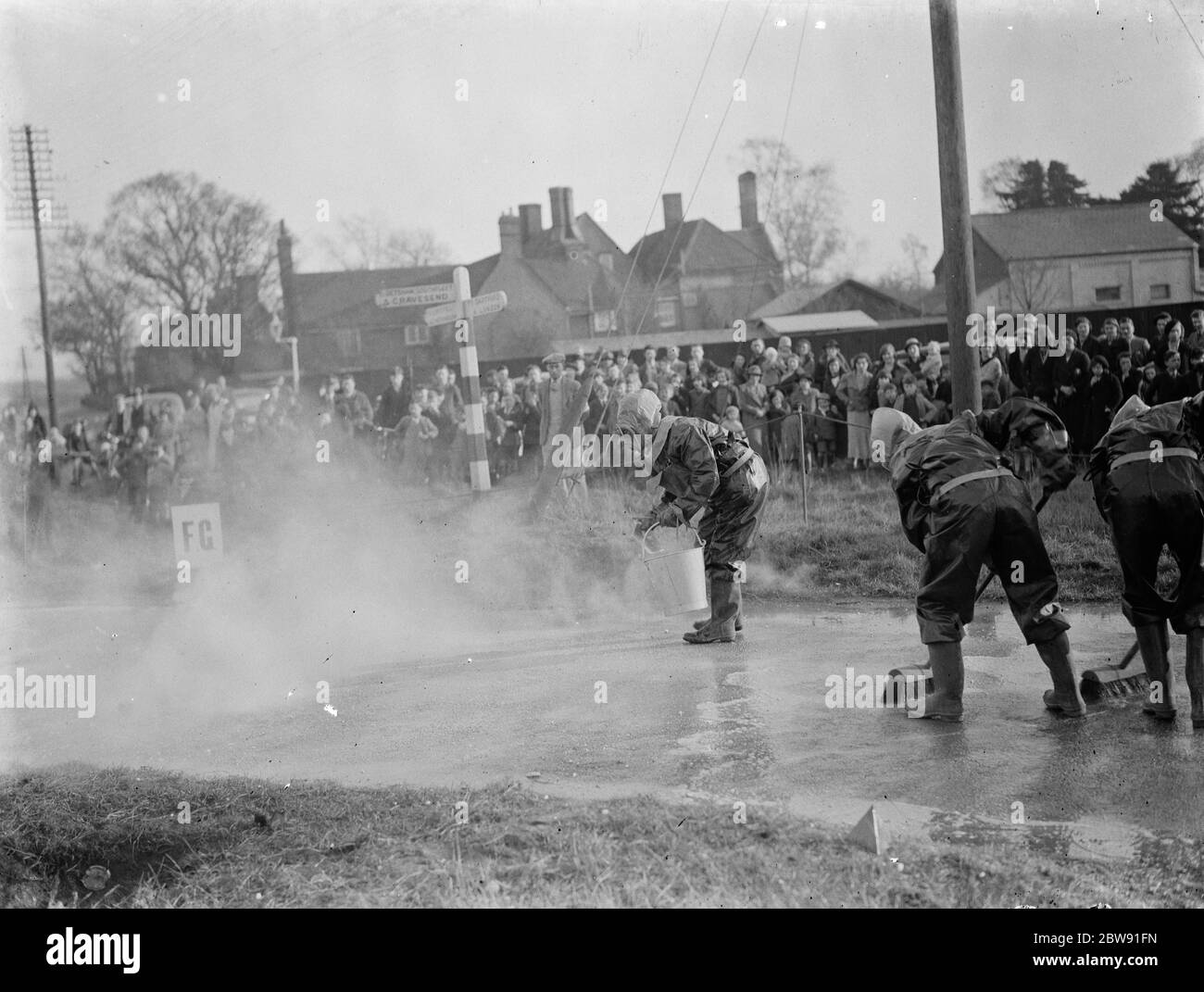 ARP (Luftangriffsvorkehrungen) Demonstrationen. Von einer Menschenmenge beobachtet, Feuerwehrleute in Green Street Green in Schutzkleidung und Gasmasken, Waschen die Straße hinunter, Dekontaminieren vermeintlichen Senfgas. März 1938 Stockfoto