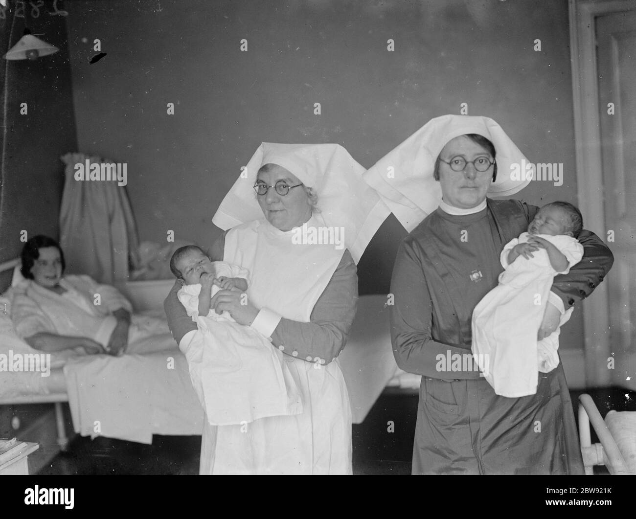 Unter den wachsamen Augen ihrer Mütter halten zwei Krankenschwestern Leap Year Babys in den Armen im Erith Mutterschaftskrankenhaus. 1936 Stockfoto