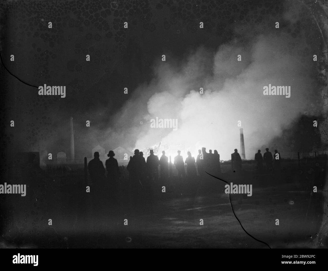 Flammen und Rauch aus einem Feuer in der Gerberei in Dartford, Kent. Die Silhouetten von einigen Zuschauern sind im Licht des Feuers umrahmt. Oktober 1939 Stockfoto