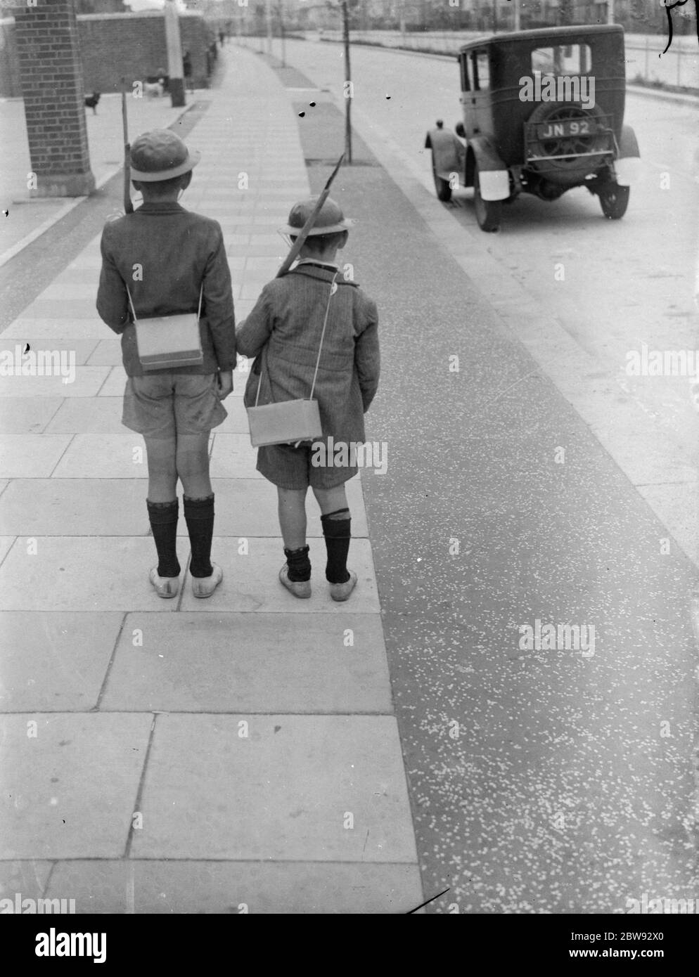 Kinder in Zinnhelmen mit Gasmaskenboxen über den Schultern spielen auf der Straße. 1939 Stockfoto