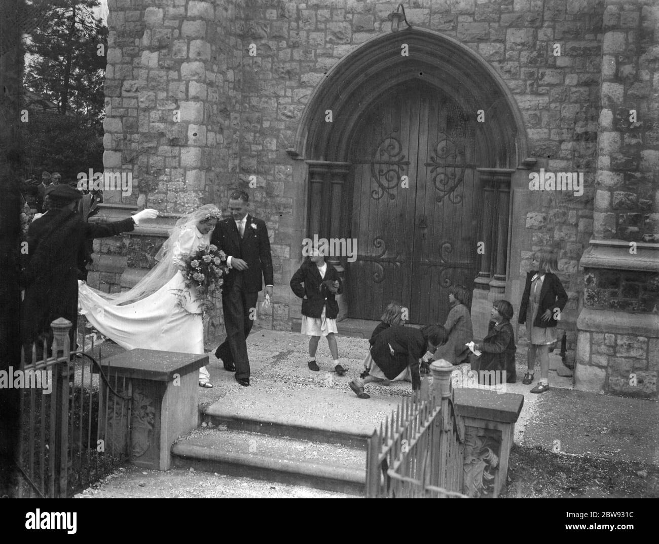 Die Hochzeit von Albert Victor Phipps und Miss Ivy Florence Morgan in Eltham, Kent. Braut und Bräutigam gehen durch das Konfetti, das die Kinder von den Stufen abholen. 1939 Stockfoto