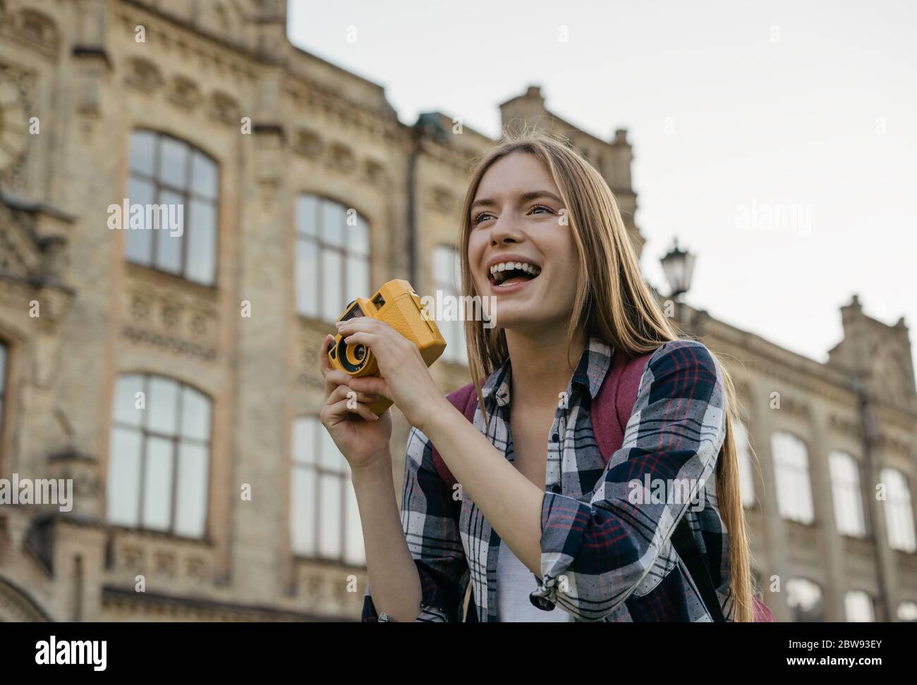 Junge Frau Tourist Foto auf Retro-Kamera. Porträt eines professionellen Fotografen mit gelber Kamera Stockfoto