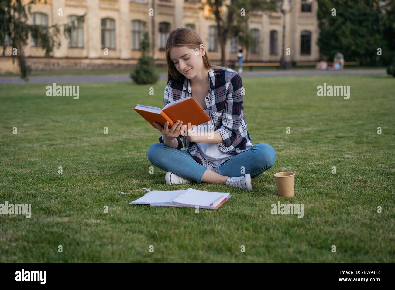 Student studieren, ein Buch lesen, Sprache lernen, Prüfungsvorbereitung, auf Gras sitzen. Bildungskonzept Stockfoto