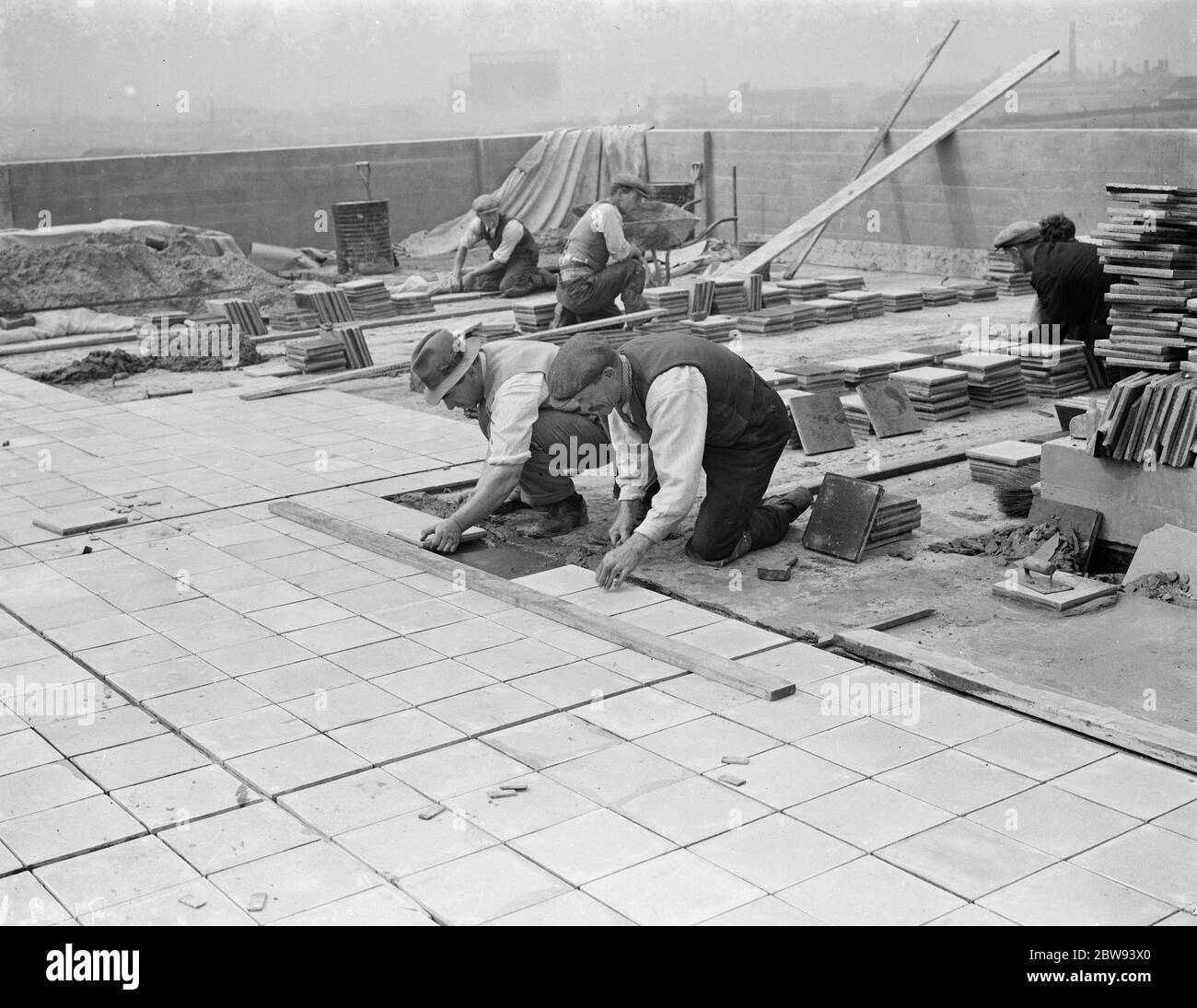 Arbeiter von Val De Travers Asphalt Limited, ein Pflasterunternehmen, arbeiten auf einem Dach in Greenwich, London. 1938 Stockfoto