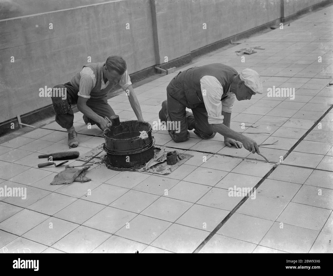 Arbeiter von Val De Travers Asphalt Limited, ein Pflasterunternehmen, arbeiten auf einem Dach in Greenwich, London. 1938 Stockfoto