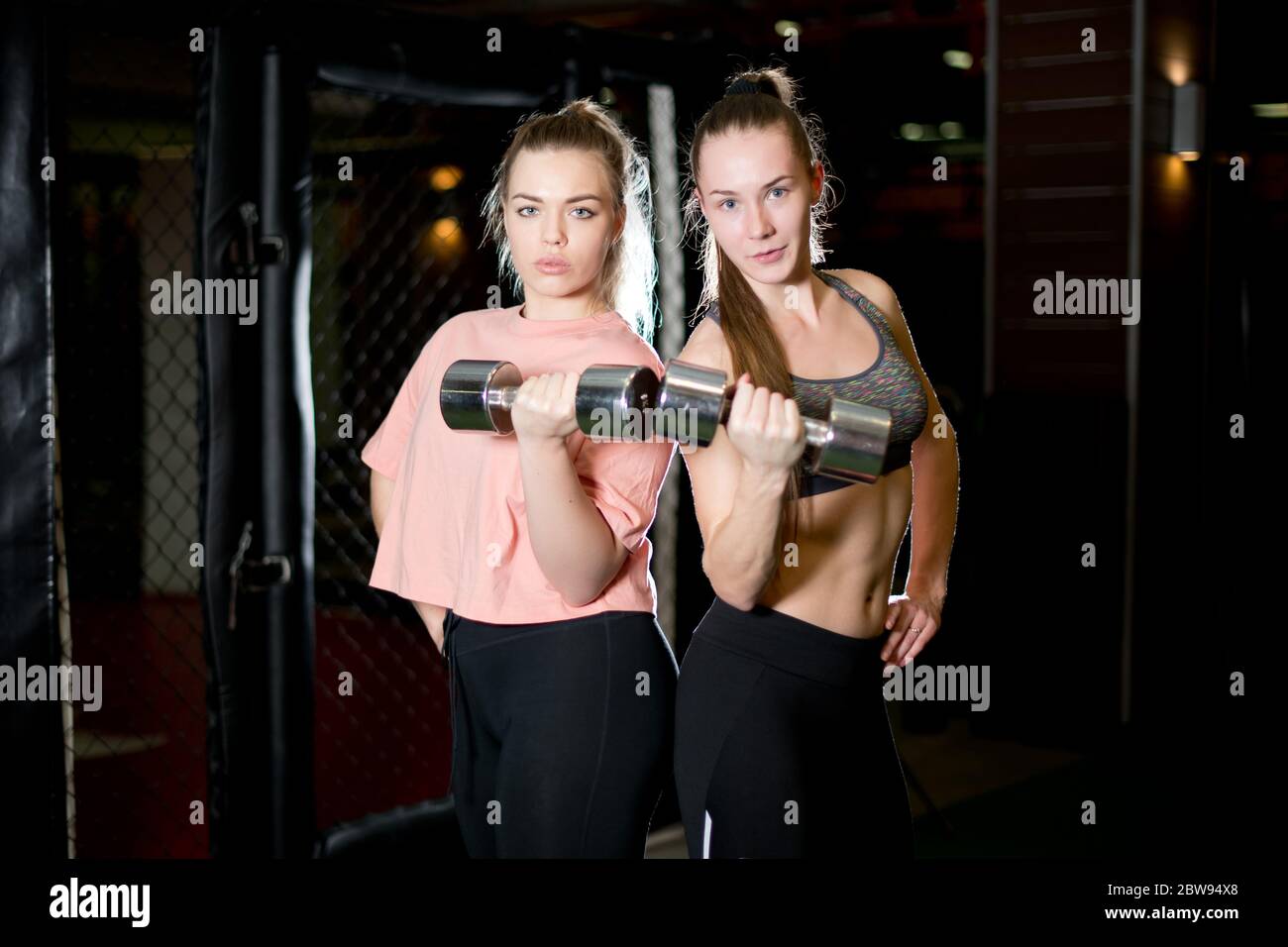 Freundinnen mit Hanteln in einem Fitnessclub, die sich die Kamera angucken Stockfoto